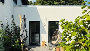 A modern house with a white exterior, a hanging chair, and a small garden area with potted plants and a lawn. - Vacation apartment Berlin city limits - between metropolis and nature (Schöneiche bei Berlin)