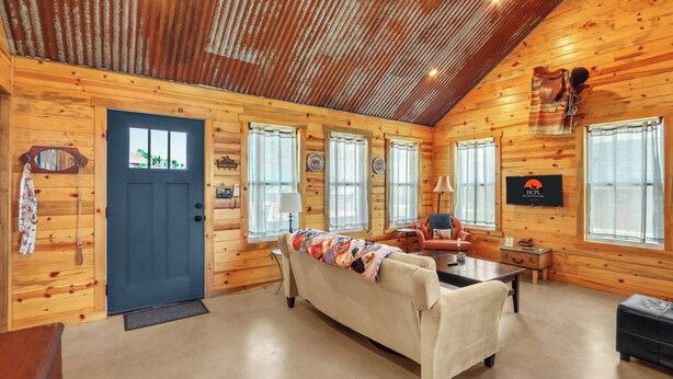 A log cabin interior with a sofa, a television, and a wooden ceiling. - RusTx Ranch Cottages 1-3 | Listing Includes 3 Cottage Rentals (Wimberley)