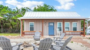 A small building with a metal roof and a blue door, surrounded by Adirondack chairs and a fire pit. - RusTx Ranch Cottages 1-3 | Listing Includes 3 Cottage Rentals (Wimberley)