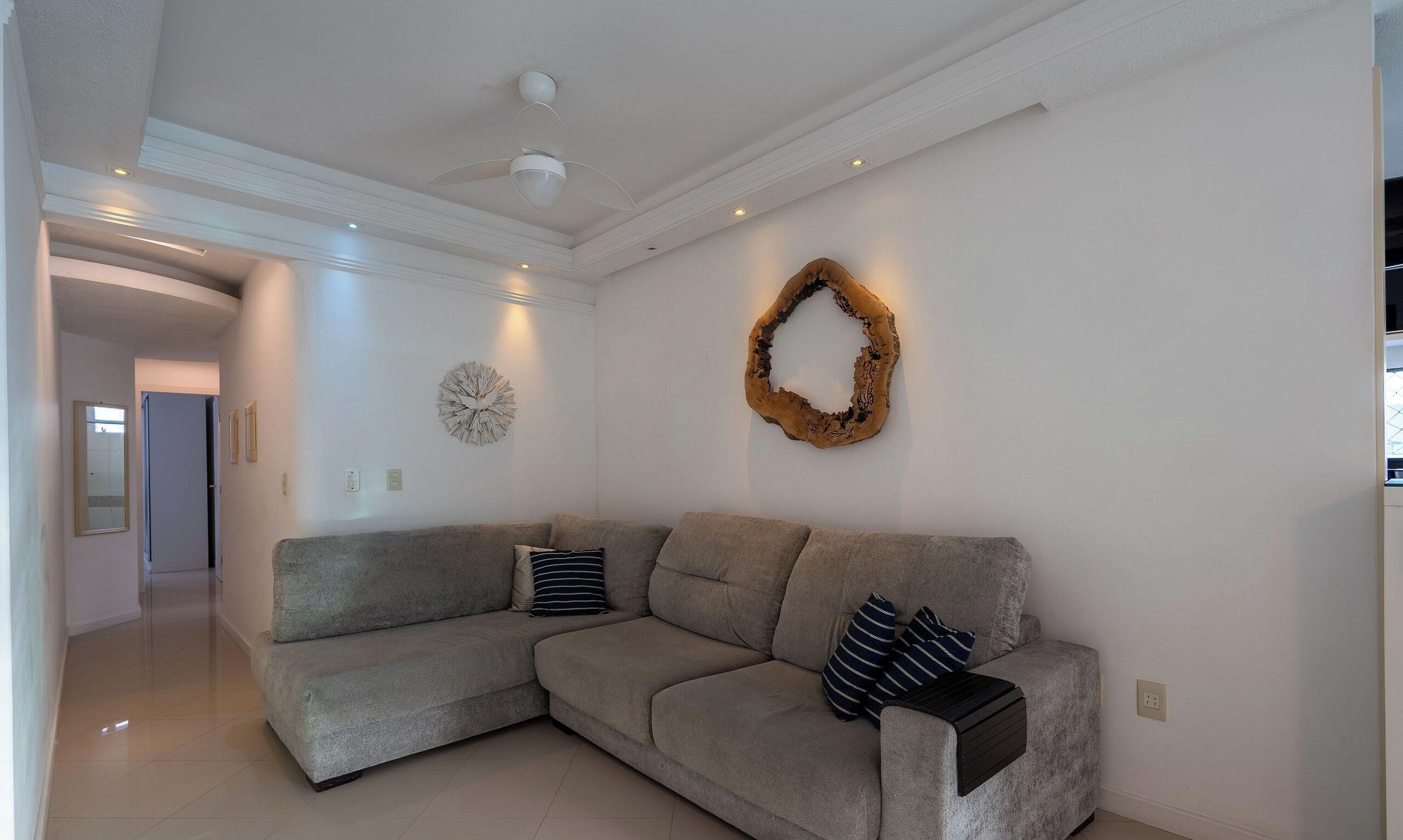 A modern living room with a grey sectional sofa, a decorative wooden wall piece, and recessed ceiling lighting.