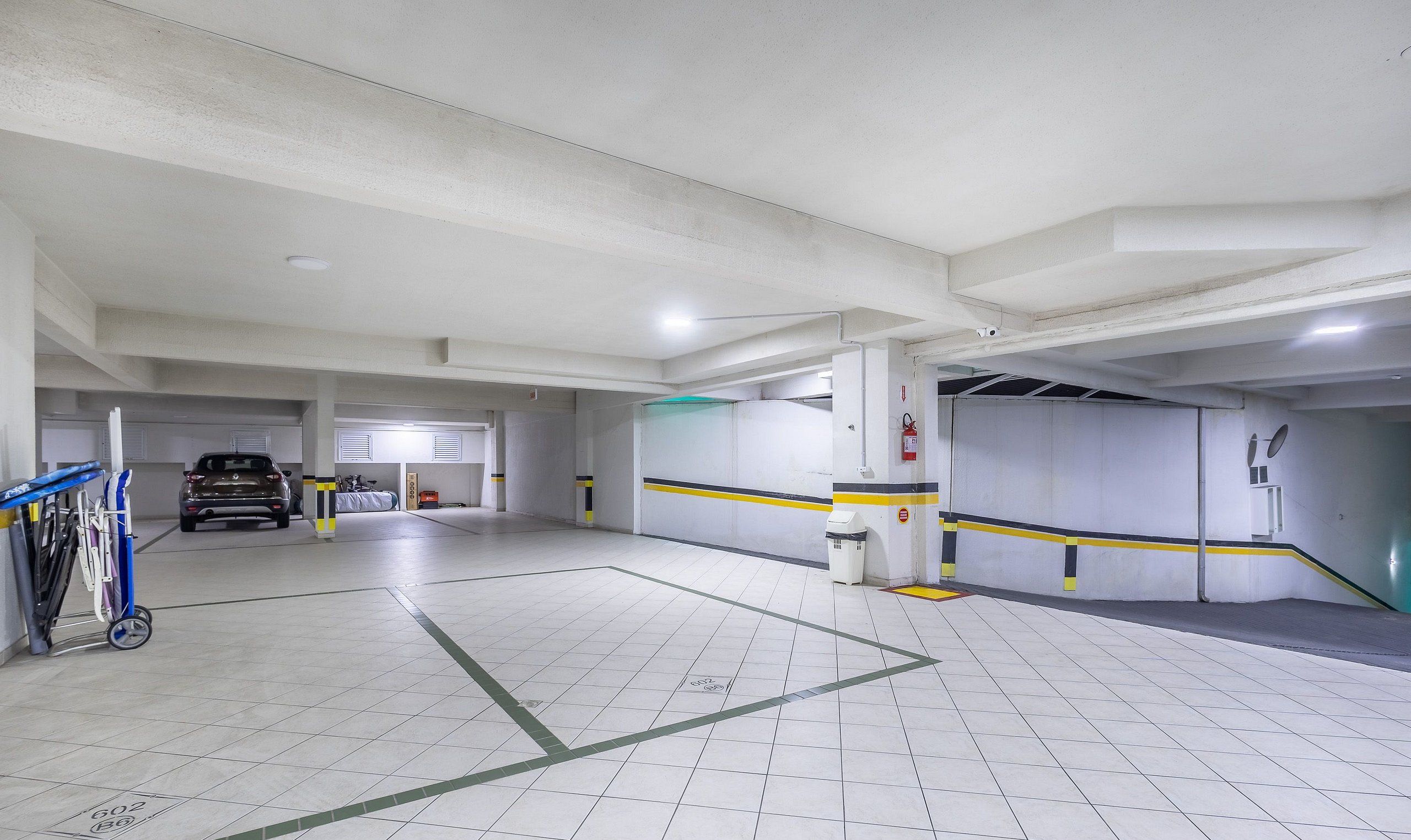 Un parking avec un sol carrelé de carreaux blancs, des places de stationnement délimitées et un extincteur fixé au mur.