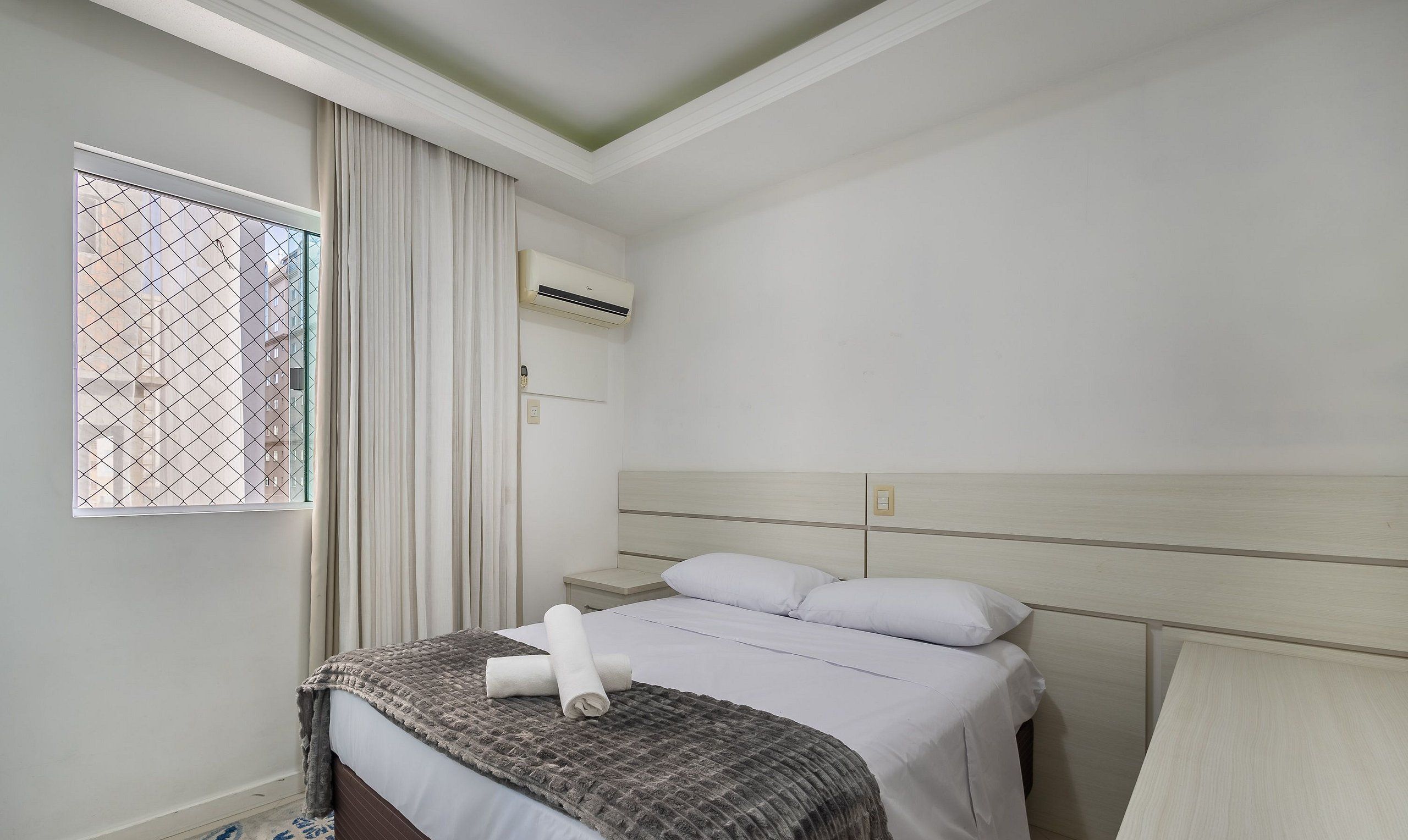 Une chambre d’hôtel avec un lit, une table de chevet, un appareil de climatisation et une fenêtre avec des rideaux.