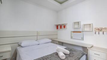 Quarto bem arrumado com uma cama, mesa de cabeceira, cômoda e prateleira na parede com caixas vermelhas e brancas.