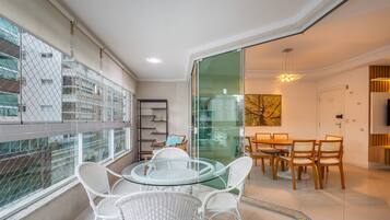 Um apartamento moderno com varanda, sala de jantar com mesa de vidro e sala de estar com televisão.