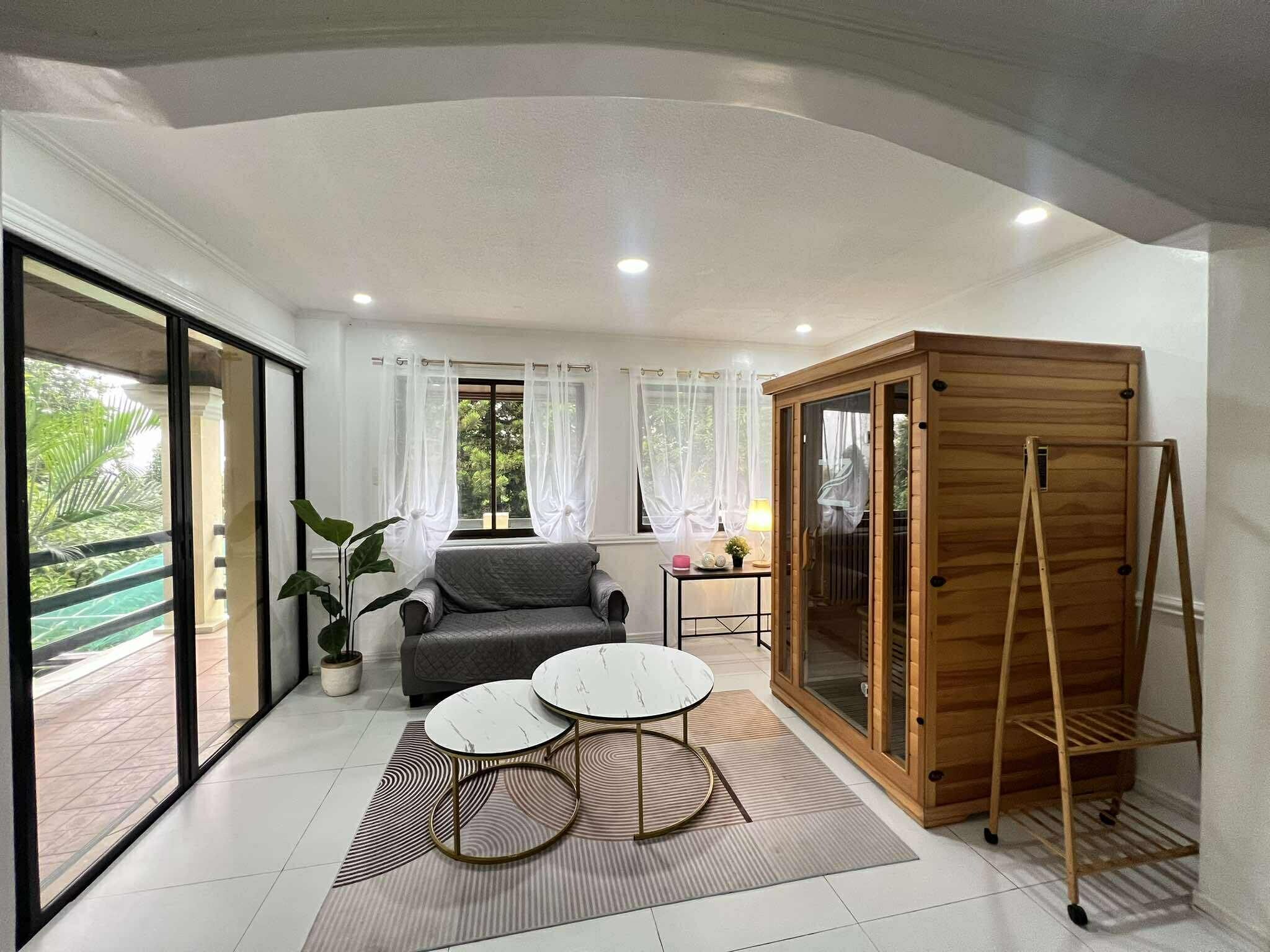 A modern living room with a sofa, two round tables, a wooden cabinet, and a large sliding glass door leading to an outdoor area.