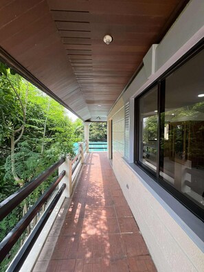 A covered walkway with a metal railing, leading to a building with large windows.