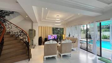 Een ruime woonkamer met een trap, een televisie en uitzicht op het zwembad.
