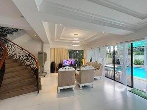 A spacious living area with a staircase, a television, and a poolside view.