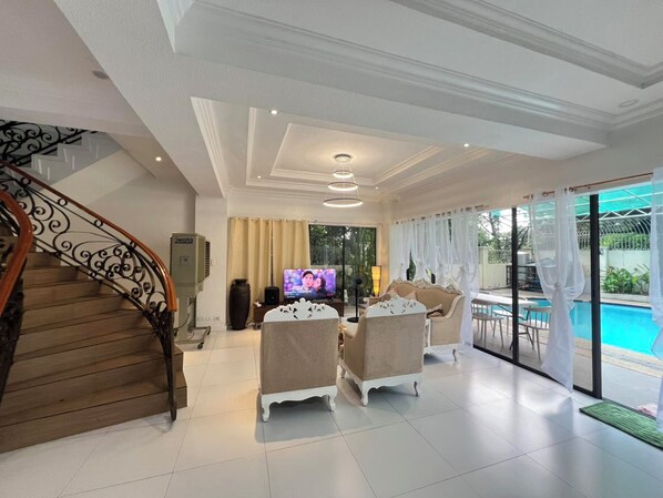 A spacious living area with a staircase, a television, and a poolside view.