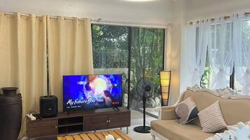 Een woonkamer met een televisie, bank en ventilator.