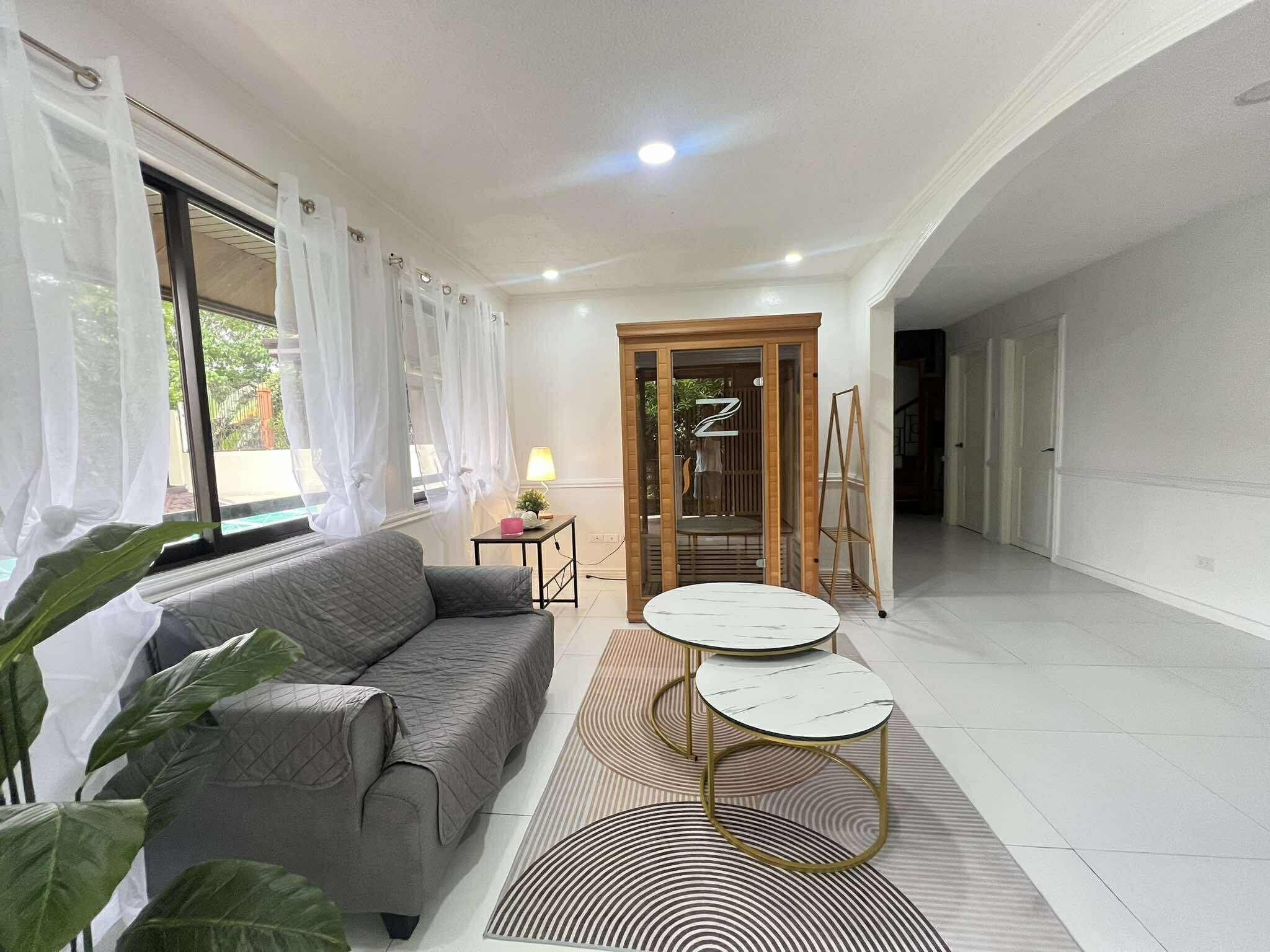 A modern living room with a grey sofa, two round tables, and a wooden door leading to another room.