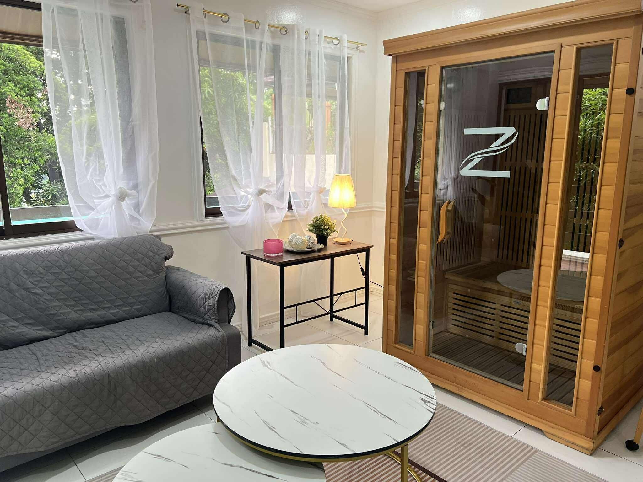 A room with a grey sofa, a round white table, a lamp, and a sliding glass door with a wooden frame.