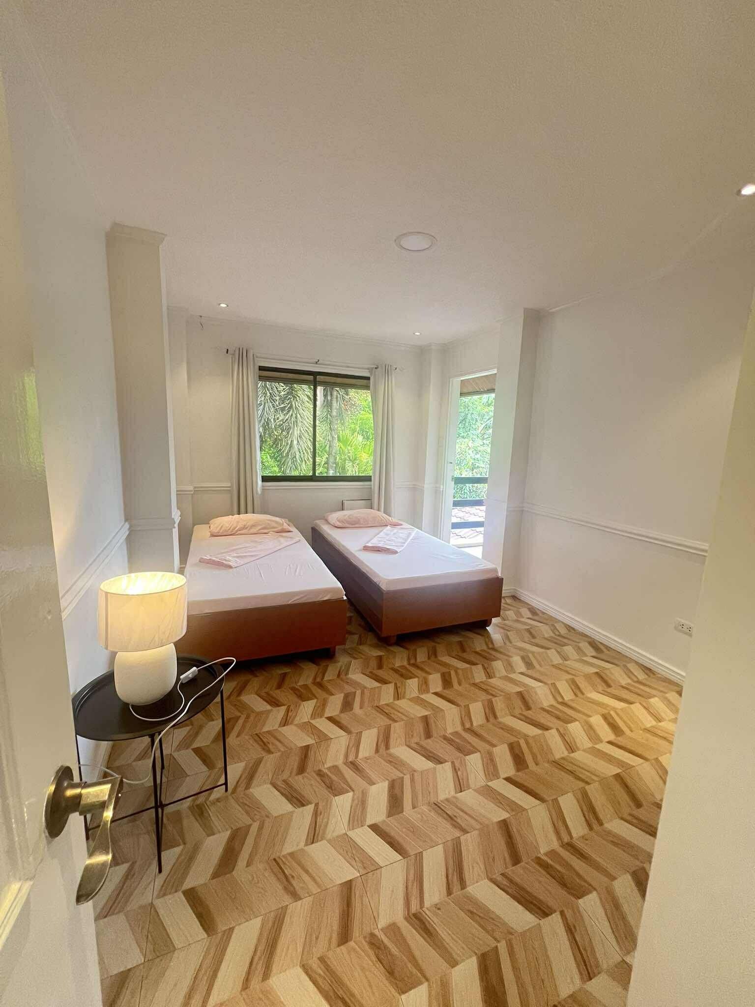 A hotel room with two beds, a desk with a lamp, and a herringbone-patterned floor.