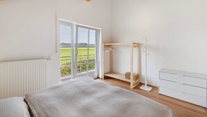 A bedroom with a bed, a white dresser, a wooden floor, a window with a view, and a balcony. - Apartment 'Monte Fiori' with Balcony and Wi-Fi (Anzing)