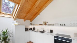 A modern kitchen with white cabinets, a wooden ceiling, a built-in oven, and a window overlooking trees. - Apartment 'Monte Fiori' with Balcony and Wi-Fi (Anzing)
