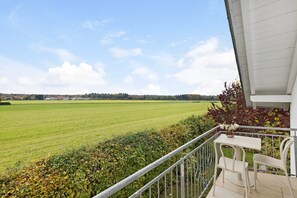 Ein Balkon mit Blick auf ein grünes Feld, einem weißen Tisch und zwei weißen Stühlen.