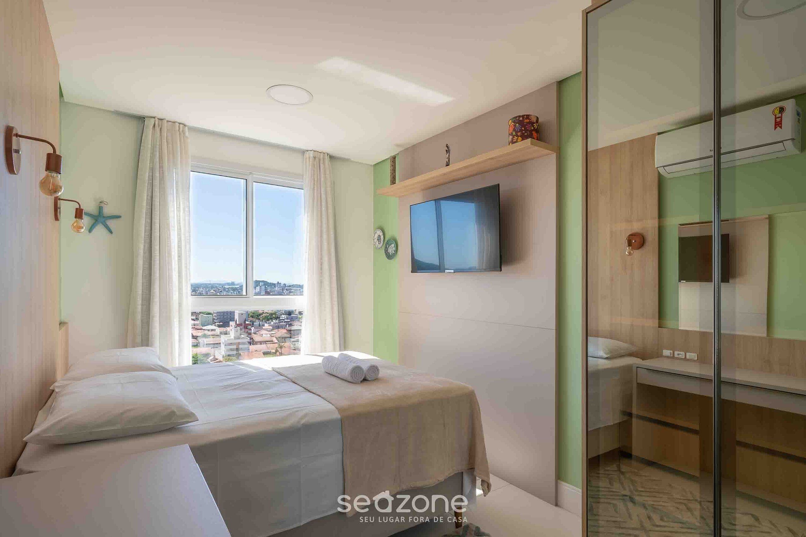 A hotel room with a bed, a television, a bathroom, and a city view.