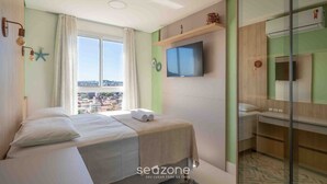 Habitación de hotel con cama, televisión instalada en la pared, ventana con cortinas y vistas a la ciudad.