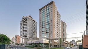Un edificio de gran altura con varios pisos y balcones, rodeado de otros edificios y una calle con coches.
