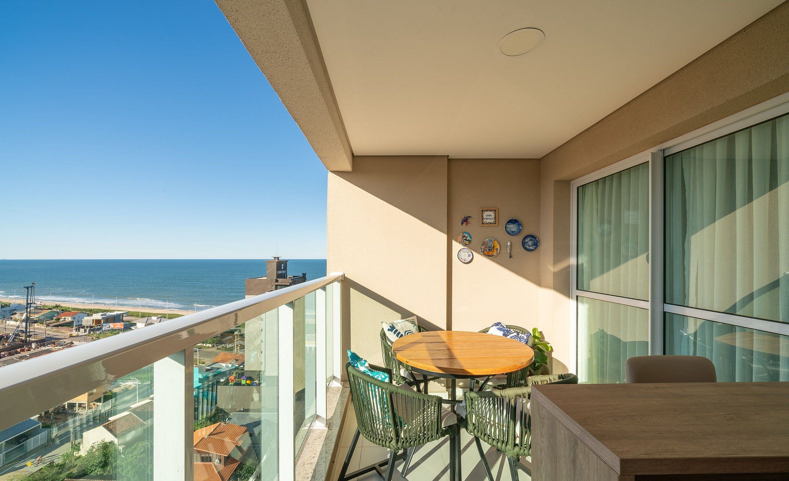 Een balkon met een houten tafel en stoelen, met uitzicht op een strand en stadsgezicht.