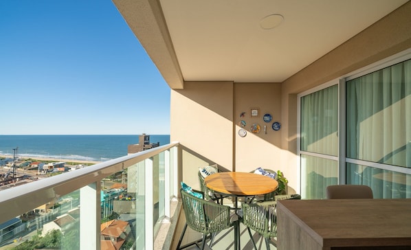 Un balcon avec une table et des chaises en bois, donnant sur une plage et offrant une vue sur la ville.
