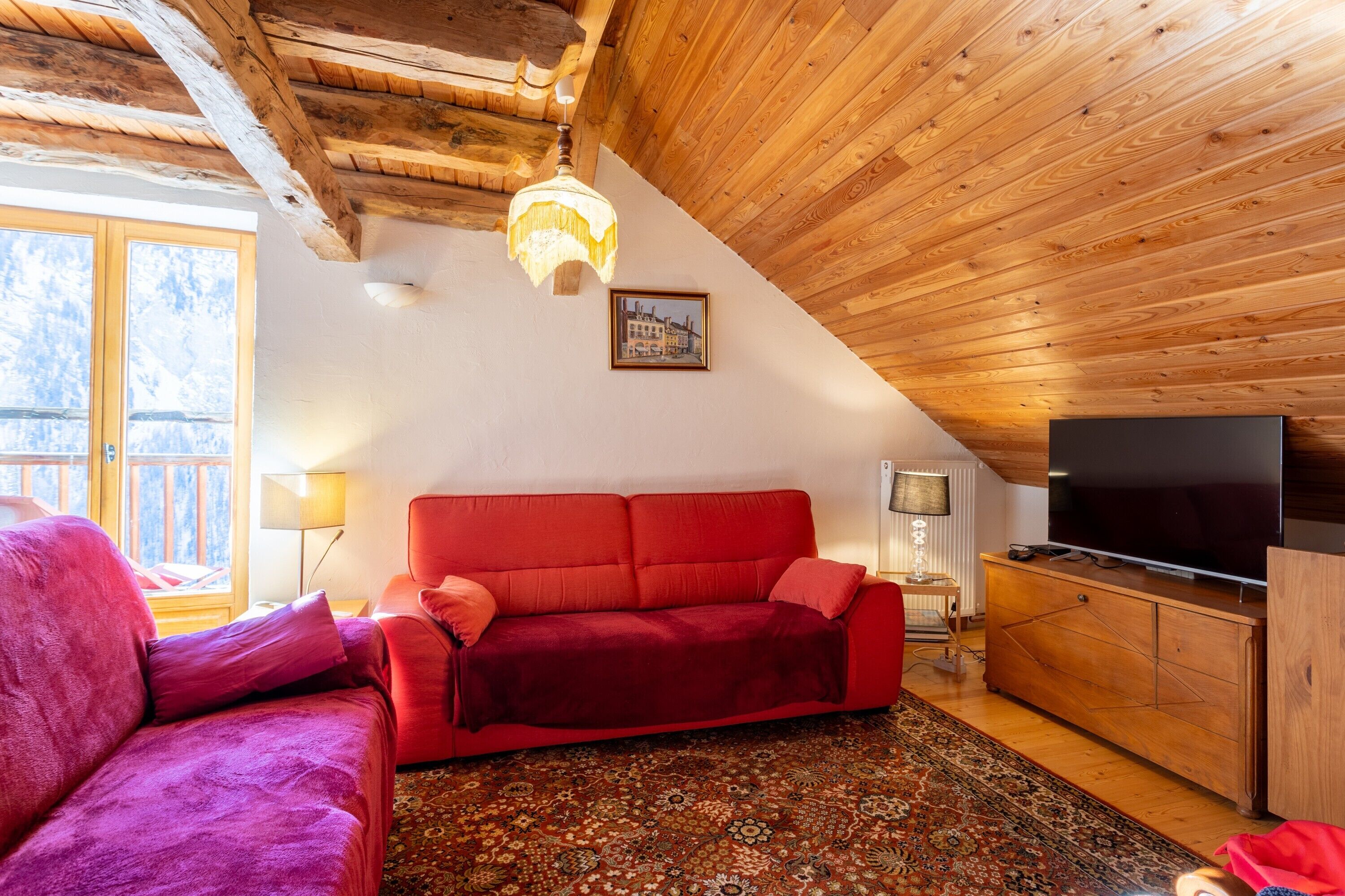 Ein gemütliches Wohnzimmer mit einem roten Sofa, Holzboden und einem Fernseher.