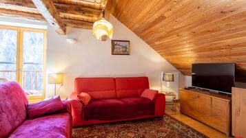 Ein gemütliches Wohnzimmer mit einem roten Sofa, Holzboden und einem Fernseher.