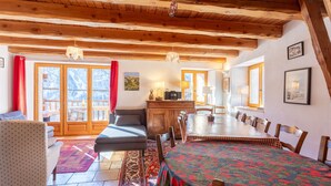 Un espace repas doté d’une grande table, de poutres en bois au plafond et offrant une vue à travers des portes vitrées.
