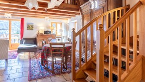 Un escalier en bois, un coin repas avec une table et des chaises, et une vue sur les montagnes à travers de grandes fenêtres.