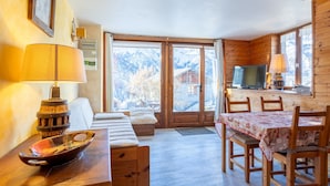 Een houten interieur met een bed, een tafel, een televisie en uitzicht op bergen.