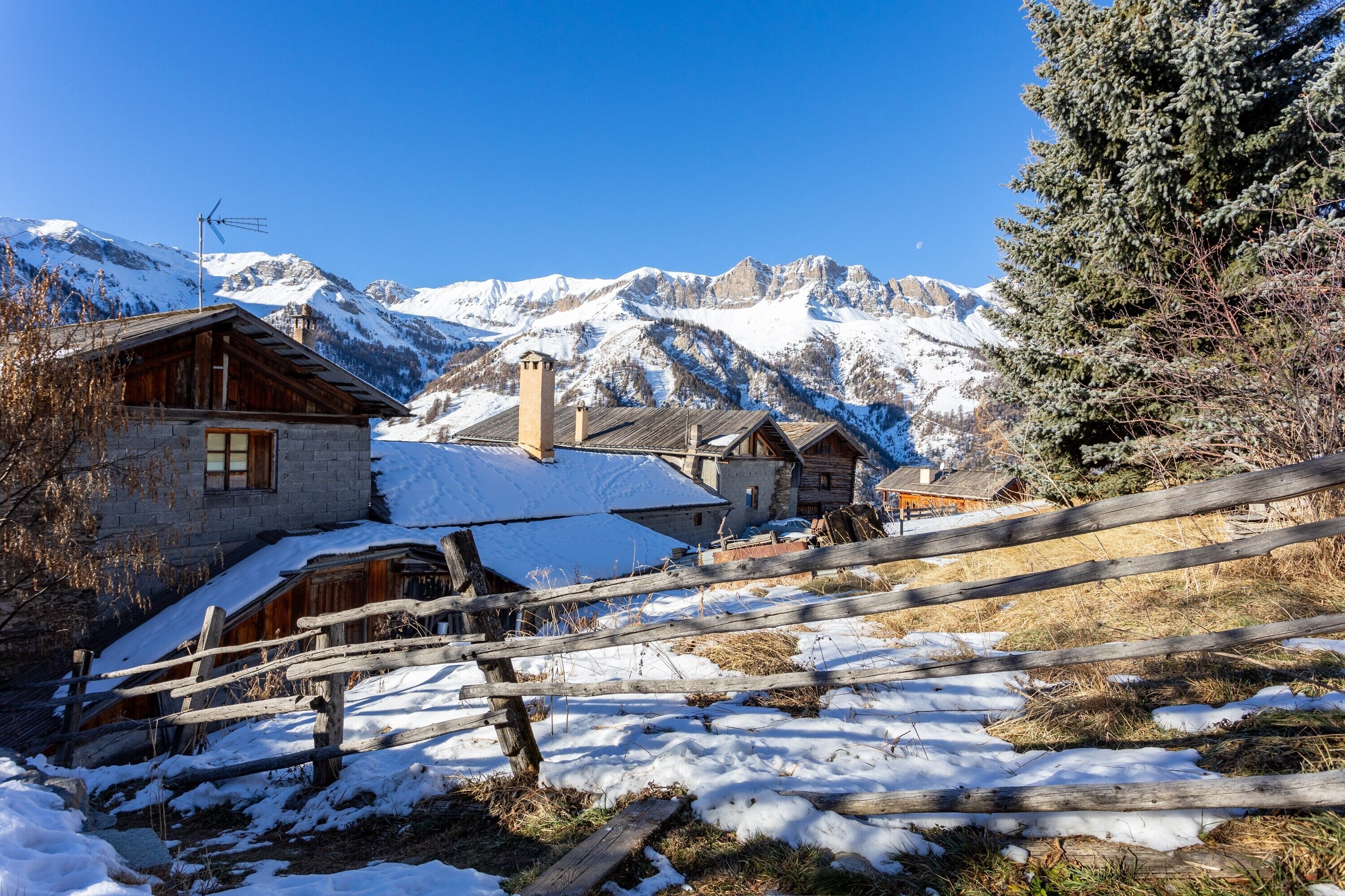 A mountain village with snow-covered buildings and a wooden fence.