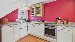 Una cocina con armarios blancos, pared roja, horno empotrado y cafetera.