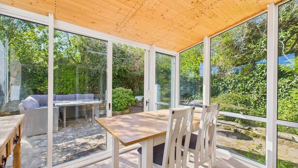 Un patio cubierto con una mesa y sillas, amplias ventanas de vidrio y vistas al verdor.