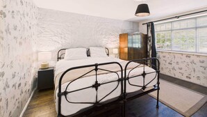 Un dormitorio con cama, mesita de noche, lámpara y ventana con persianas.