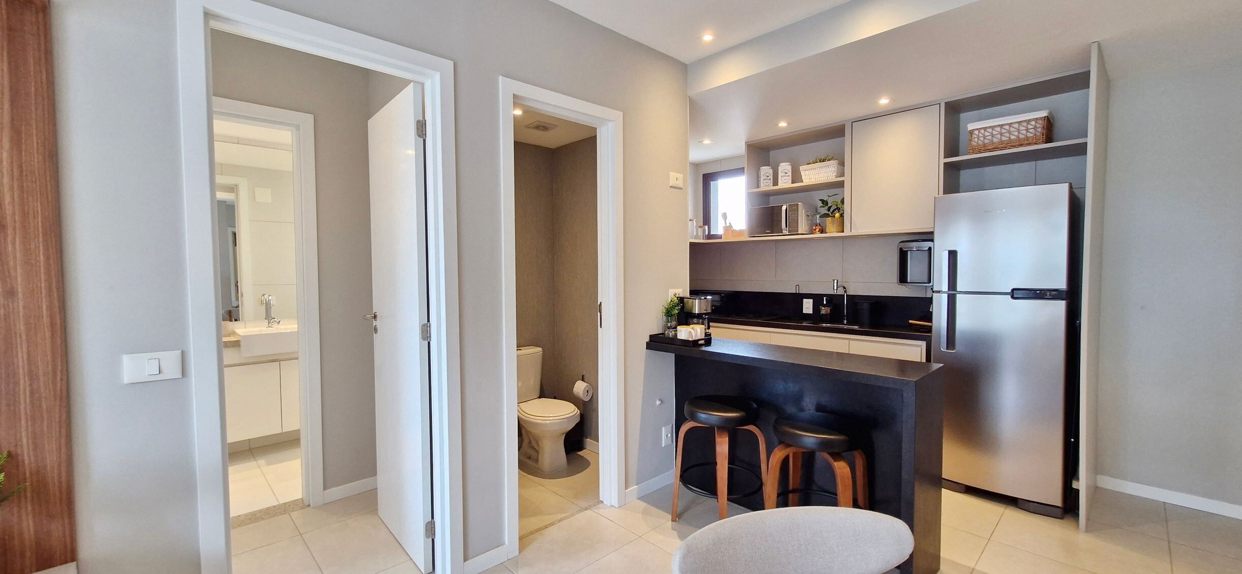 A compact kitchen with a refrigerator, microwave, and bar stools.