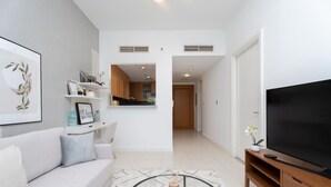 A modern living room with a sofa, a coffee table, a TV, and a kitchen visible through an open door. - Serene 1BR at Iris Blue Marina (Dubai)