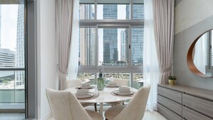 A dining area with a table set for two, a view of tall buildings, and a large window with curtains. - Serene 1BR at Iris Blue Marina (Dubai)