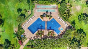 Eine Vogelperspektive zeigt einen luxuriösen Urlaubsort mit zwei großen Schwimmbecken, einem Shuffleboardplatz und üppiger, grüner Vegetation.