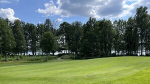A well-maintained golf course with a clear path, surrounded by dense trees and a body of water in the background.
