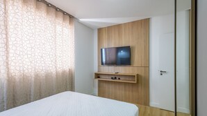 A bedroom with a bed, a TV mounted on a wooden panel, and a door. - 3-suite apt 280m From sea in Itapema Vga1002 (Itapema)