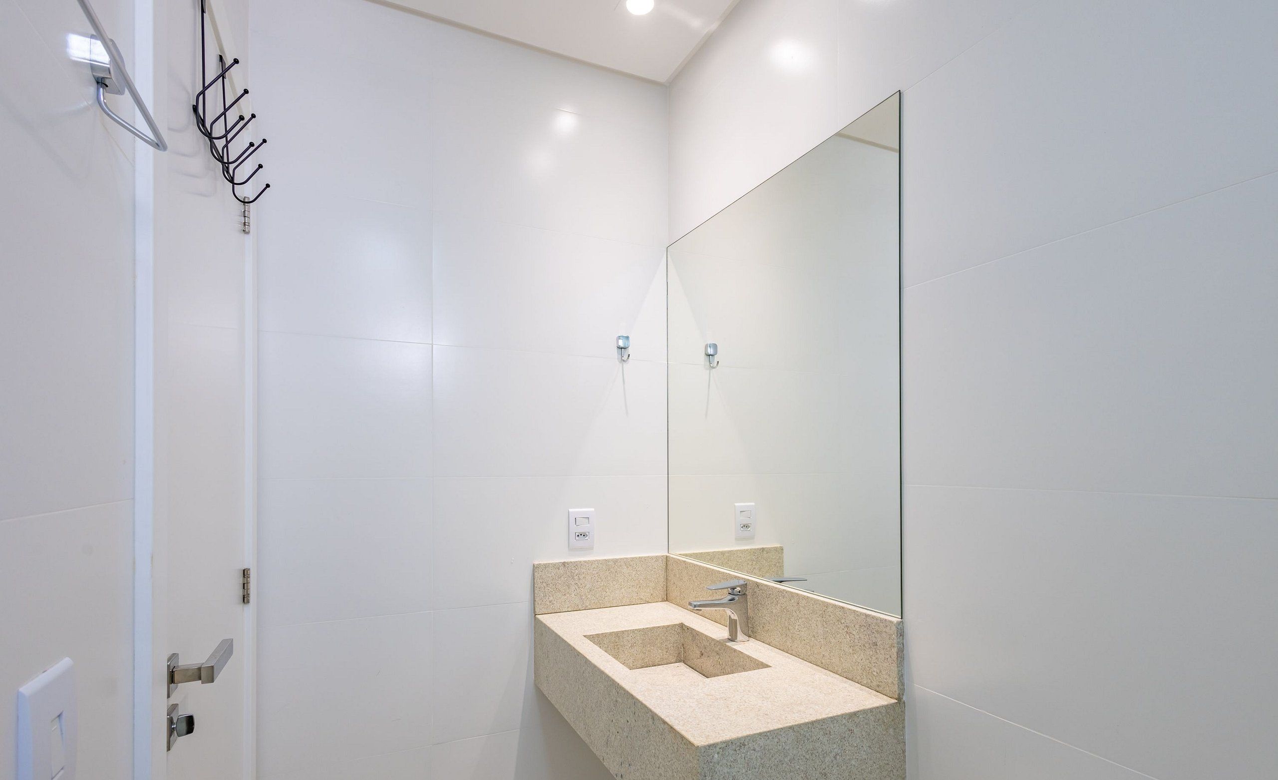 Un baño moderno con un lavabo rectangular, un espejo grande y un perchero para toallas.