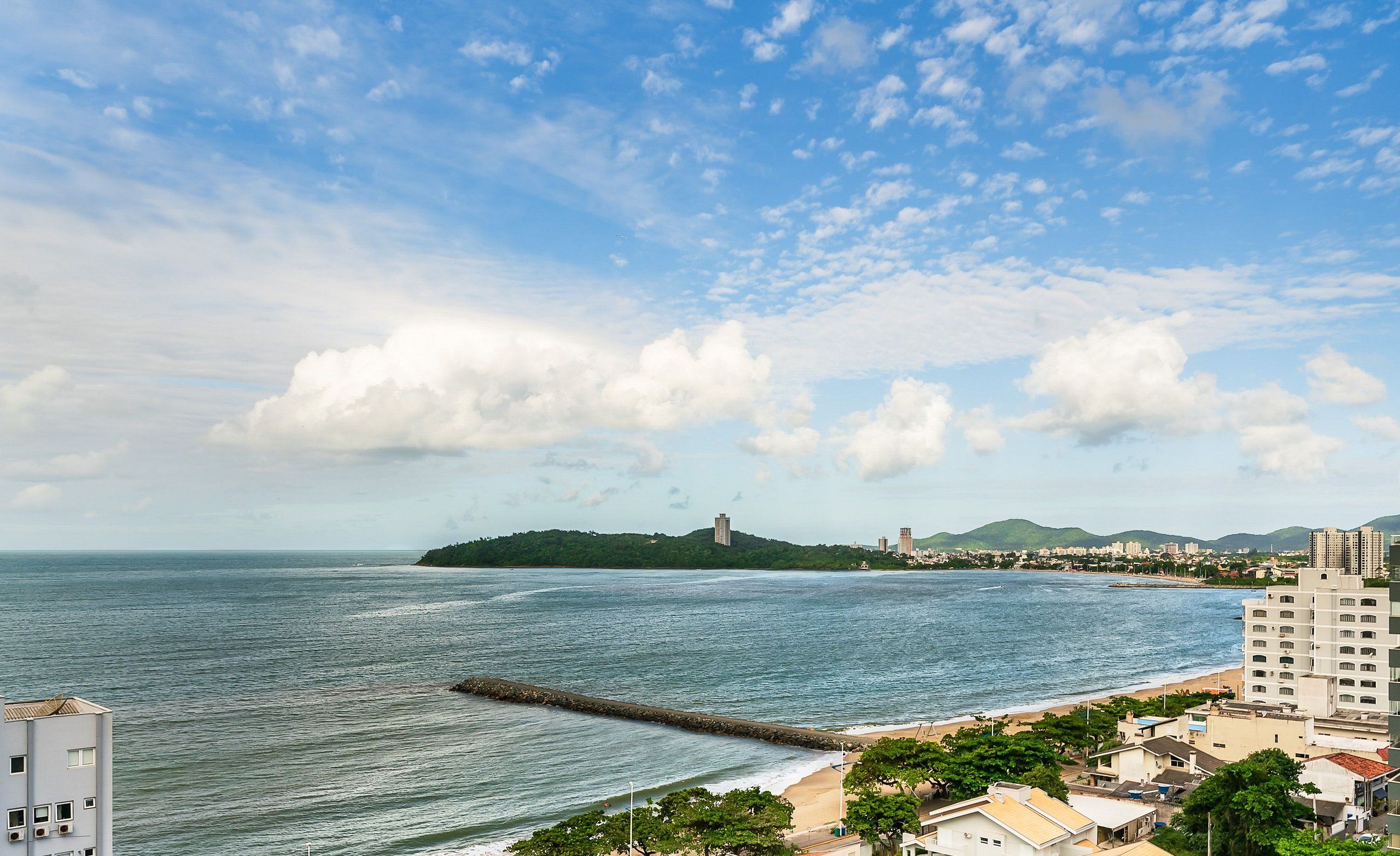 A coastal cityscape with a beach, buildings, and a prominent hill with a tower.