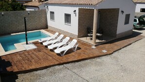 Une petite maison avec une piscine, des chaises longues blanches et un espace patio.