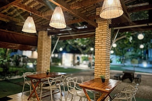 Un espacio de comedor al aire libre con pilares de ladrillo, mesas de madera y sillas blancas.