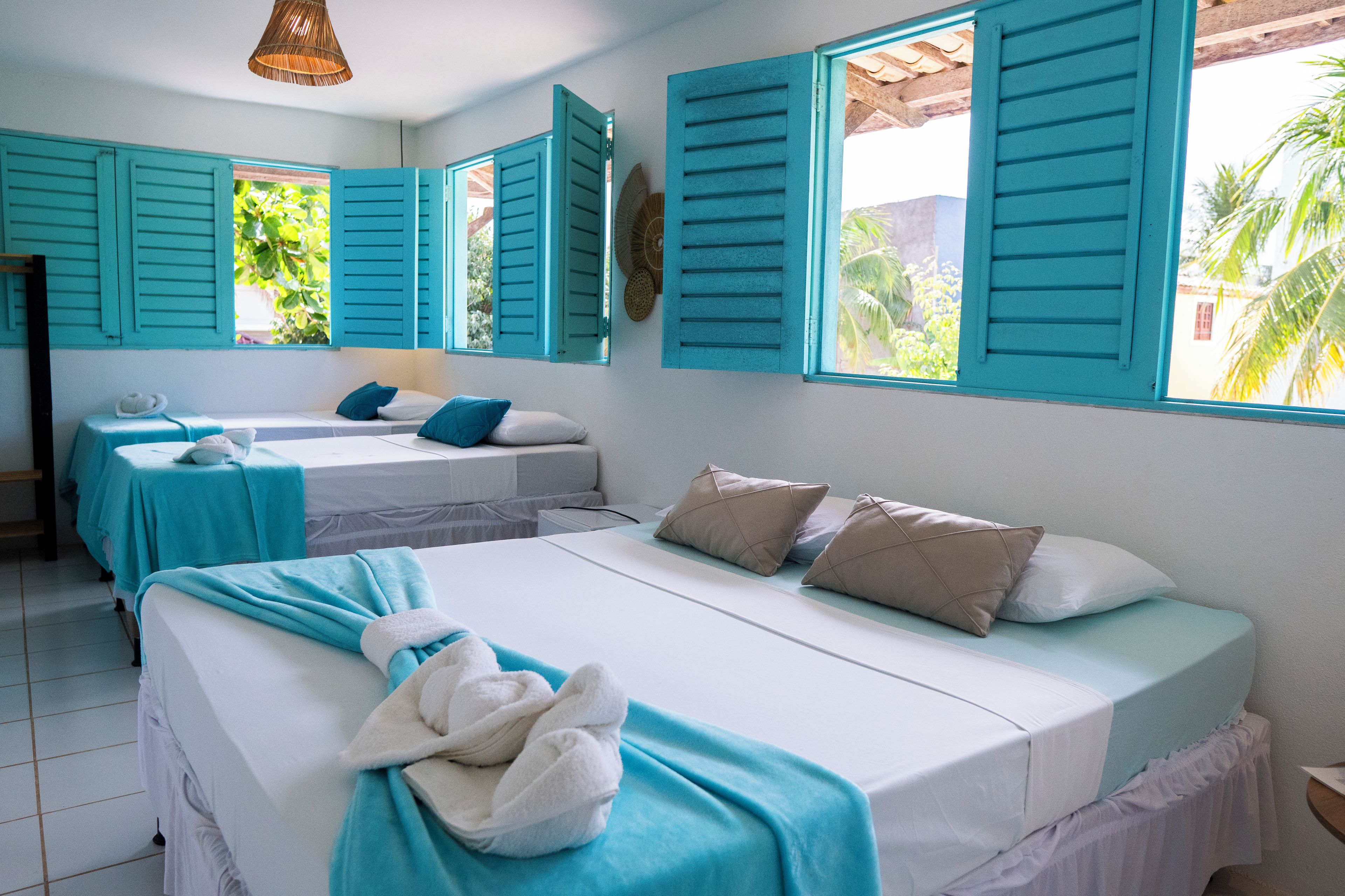 Habitación de hotel con dos camas, contraventanas color turquesa y vistas a zonas verdes.