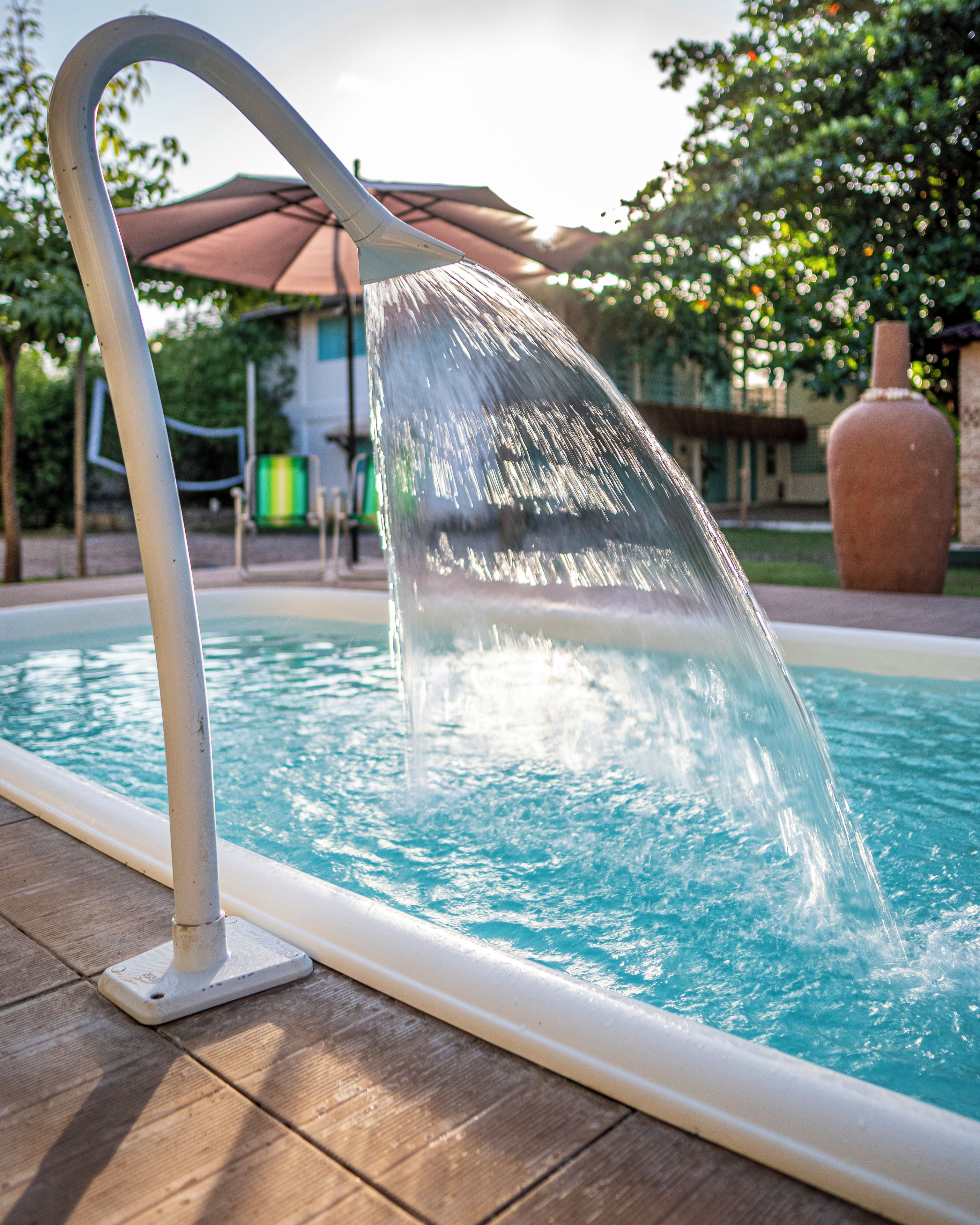 A pool with a water feature, a wooden deck, and a building in the background.