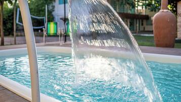 A pool with a water feature, a wooden deck, and a building in the background.