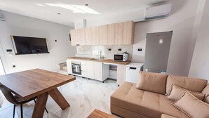 Een moderne keuken met witte kastjes, een magnetron en een inbouwoven. In de woonruimte staat een houten eettafel en een beige bank.