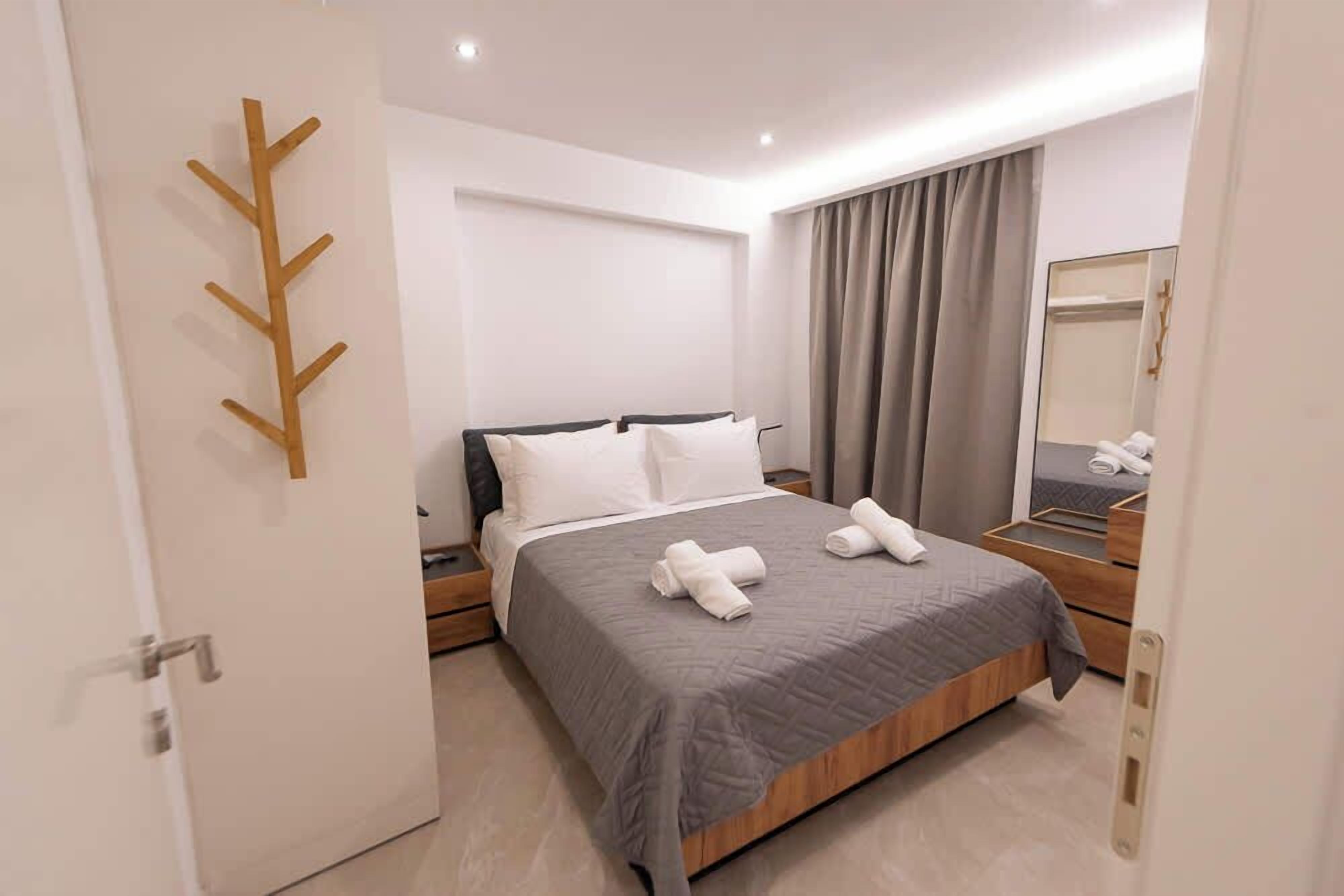 Een moderne hotelkamer met een opgemaakt bed, een houten kapstok, een grote spiegel en uitzicht op de stad door het raam.