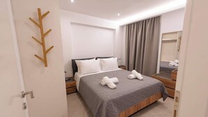 Een moderne hotelkamer met een opgemaakt bed, een houten kapstok, een grote spiegel en uitzicht op de stad door het raam.
